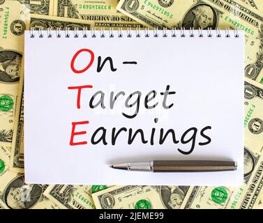 OTE-Symbol für die angestrebten Gewinne. Das Konzept formuliert OTE-Zielgewinne auf weißer Note auf einem schönen Hintergrund von Dollarnoten. Metallstift. Unternehmen Stockfoto