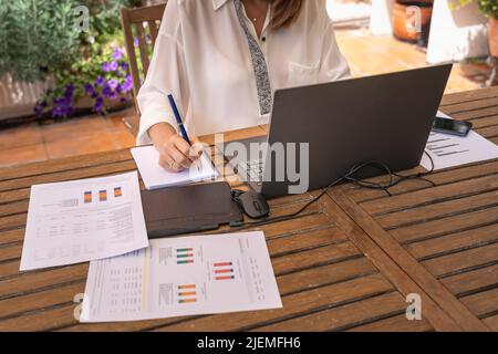 Weiße Frau, die im Garten mit Laptop und Notebook Telearbeit verführt. Stockfoto