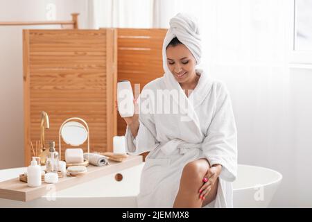 Fröhliche Frau Im Bademantel Zeigt Shampoo-Flasche Im Modernen Badezimmer Stockfoto