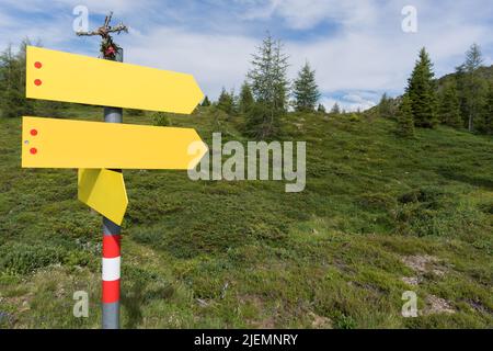 Gelbe, deutlich sichtbare Wegweiser in verschiedene Richtungen in alpinem Gelände mit überwucherten Bergen und teilweise bewölktem, blauem Himmel als Hintergrund Stockfoto