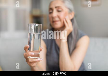 Unglücklich traurige europäische alte Frau mit grauen Haaren halten Glas Wasser, leidet unter Schmerzen Stockfoto