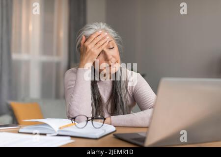 Depressive müde europäische reife Frau mit grauem Haar leidet unter Kopfschmerzen, bekam Stress und unglückliches Gesicht Stockfoto