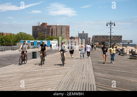 Menschen, die auf dem Riegelmann Boardwalk in Coney Island in Brooklyn, New York City, Vereinigte Staaten von Amerika, Rad fahren Stockfoto