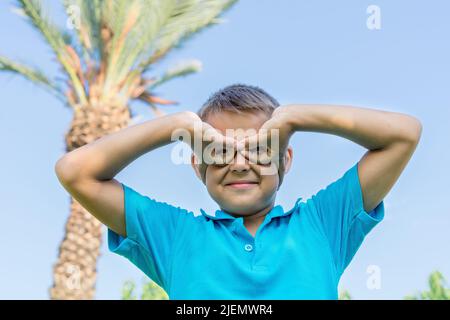 Porträt eines fröhlichen Jungen vor dem Hintergrund des Himmels und der Palmen. Stockfoto