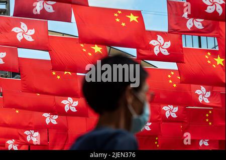 Hongkong, China. 27.. Juni 2022. Unter der Flagge der Volksrepublik China ist ein Fußgänger zu sehen, und die Sonderverwaltungszone Hongkong wird vor dem 1.. Juli, dem Jahrestag der Übergabe Hongkongs an China in Hongkong, ausgestellt. Kredit: SOPA Images Limited/Alamy Live Nachrichten Stockfoto