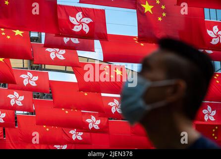 Hongkong, China. 27.. Juni 2022. Unter der Flagge der Volksrepublik China ist ein Fußgänger zu sehen, und die Sonderverwaltungszone Hongkong wird vor dem 1.. Juli, dem Jahrestag der Übergabe Hongkongs an China in Hongkong, ausgestellt. Kredit: SOPA Images Limited/Alamy Live Nachrichten Stockfoto