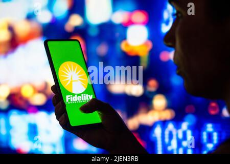 In dieser Abbildung hält eine silhouettierte Frau ein Smartphone mit dem Fidelity Investments-Logo auf dem Bildschirm. Stockfoto