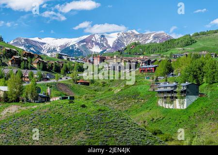 Mount Crested Butte, USA - 20. Juni 2019: Dorf Mt Crested Butte Resort im Sommer mit buntem Gras und hölzernen Unterkünften auf Hügeln mit Stockfoto