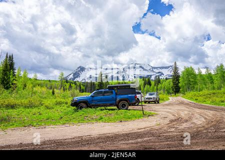 Crested Butte, USA - 22. Juni 2019: Schneebedeckter Berg und Parkplatz am Lost Lake Campground im Sommer Espenwald mit weißen Wolken durch Schmutz Stockfoto