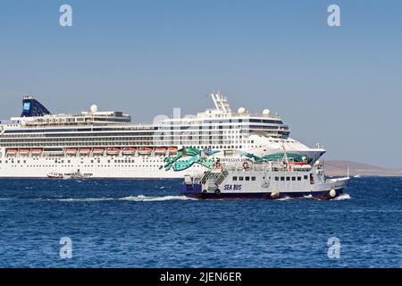 Mykonos, Griechenland - Juni 2022: Die Passagierfähre des Seebusses fährt vor dem norwegischen Jade-Schiff, das vor der griechischen Insel auf See vor Anker liegt. Stockfoto