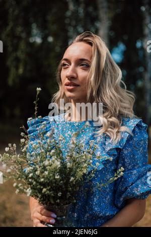 Ein junges Mädchen in einem blauen Kleid hält Wildblumen in ihren Händen Stockfoto