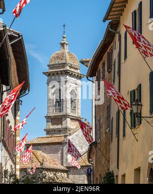 Vor dem Turm der Stiftskirche von San Quirico d'Orcia, Toskana, Italien, fliegen lokale Flaggen Stockfoto