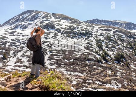 Mann mit den Armen, der mit Freiheit auf dem Linkins Lake Trail Peak auf dem Independence Pass in den felsigen Bergen in der Nähe von Aspen, Colorado, gebeugt wurde, im Frühsommer mit Sno Stockfoto