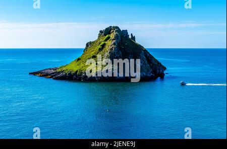 Kleines Motorboot, das Felseninsel in einem klaren blauen Meer, sonnigem blauen Himmel und ruhigem Wasser passiert und ein Wake hinter sich lässt. Vielleicht ein Fischerboot oder eine kurze Reise. Stockfoto