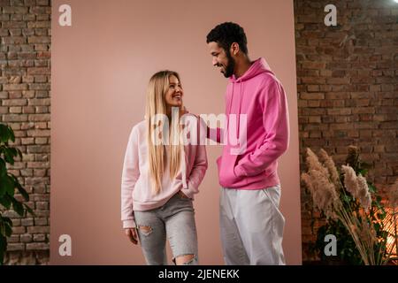 Romantisches Modestudio-Portrait eines jungen Biracial-Paares verliebt in Hoodie posiert auf rosa Hintergrund. Stockfoto