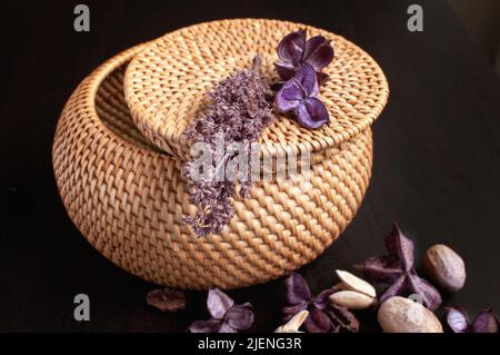 Korbrattan-Box Handwerk rund auf der Oberseite mit getrockneten Blumen und Lavendel auf schwarzem Hintergrund Stockfoto