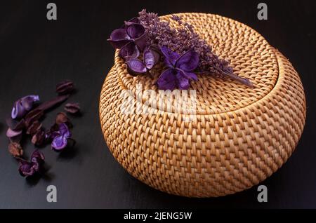 Weidenstrohbox Handwerk runden Top mit getrockneten Blumen und Lavendel auf einem schwarzen Hintergrund Stockfoto