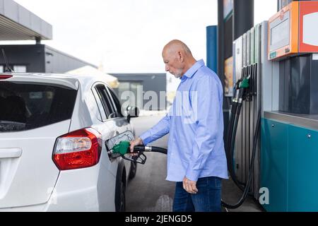 Leitender Geschäftsmann, der auf einer Tankstelle steht und ein Auto betankt. Stockfoto