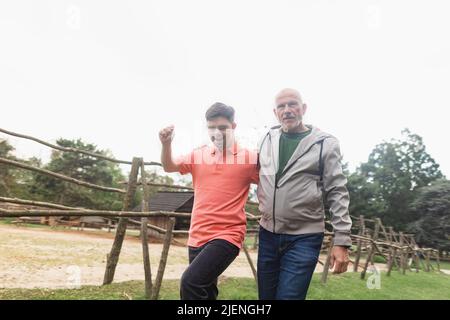 Glücklicher älterer Vater mit seinem jungen Sohn mit Down-Syndrom, der zusammen im Park läuft. Stockfoto