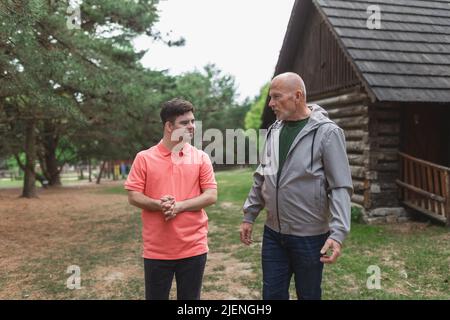 Glücklicher älterer Vater mit seinem jungen Sohn mit Down-Syndrom, der zusammen im Park läuft. Stockfoto