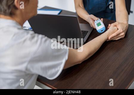 Der Arzt misst die Temperatur des Patienten mit einem berührungslosen Thermometer während eines Termins Stockfoto