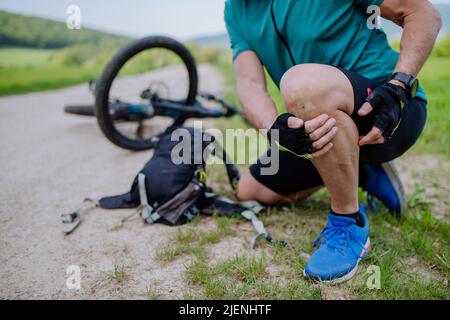Aktiver Senior in Sportkleidung fiel vom Fahrrad auf den Boden und verletzte sich im Sommer im Park sein Knie. Stockfoto