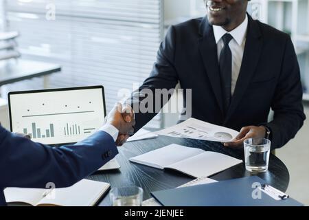 Nahaufnahme von zwei unpersönlichen Geschäftsleuten, die sich nach der Verhandlung über den Besprechungstisch im Büro die Hände schüttelten Stockfoto