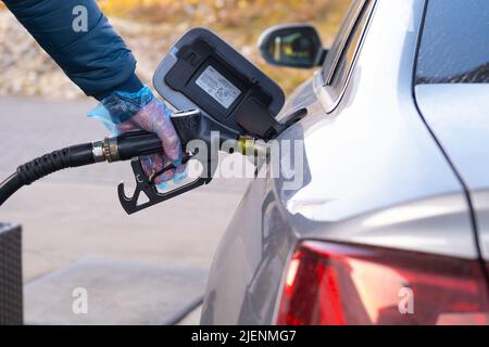 Kraftstoffpreis in Europa. Tanken des Autos.Betanken der Pistole in den Händen eines Mannes in einem Handschuh.Auto an einer Tankstelle. Silber Auto, Betankungspistolen und Stockfoto