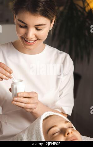 Die Kosmetikerin, die Creme auf das Gesicht des Patienten applyte, war mit den Leistungen des Schönheitssalons zufrieden. Heller Hintergrund. Peeling Verjüngung. Gesichtsbehandlung Stockfoto