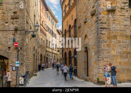 Touristen und Italiener genießen eine der engen verwinkelten Gassen durch das mittelalterliche Zentrum der Hügelstadt Volterra in Italien in der Toskana. Stockfoto