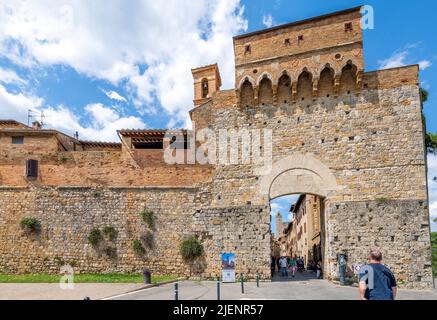 Die Außenmauer der Hauptfußgängerzone, gefüllt mit Geschäften und Cafés, führt durch die mittelalterliche Hügelstadt San Gimignano, Italien, in der Toskana. Stockfoto