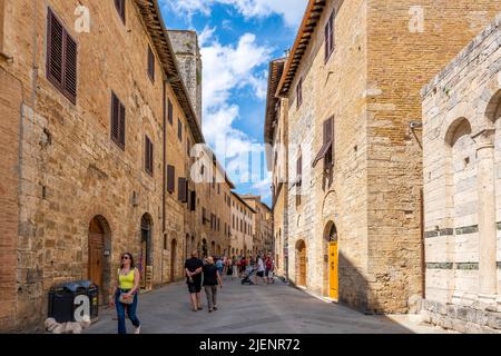 Touristen wandern durch die enge Hauptfußgängerzone voller Geschäfte und Cafés durch die mittelalterliche Hügelstadt San Gimignano, Italien, in der Toskana. Stockfoto