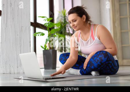 Eine Frau mittleren Alters mit Kopfhörern bereitet sich auf das Training im Internet vor. Sie sucht in den Tutorials nach Übungsvideos. Nahaufnahme. Stockfoto