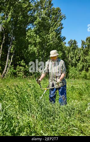 Ein Mann mäht das Gras auf dem Feld mit einem Trimmer. Gartenpflege-Konzept. Vertikales Foto. Stockfoto