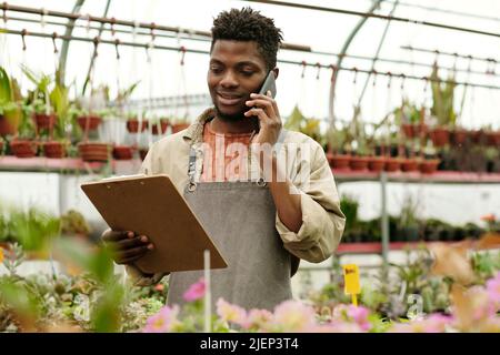 Der Besitzer eines Blumenshopfs sieht sich das Dokument in seinen Händen an und nimmt eine Bestellung vom Kunden per Mobiltelefon an Stockfoto