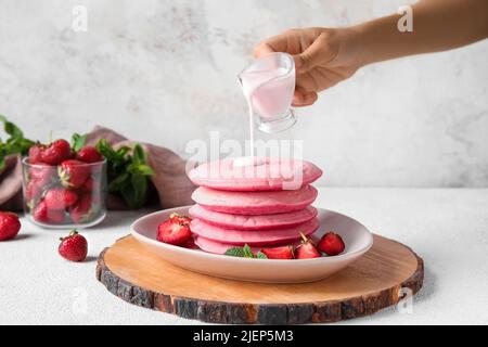 Frau gießt Sauce auf rosa Pfannkuchen auf hellem Hintergrund Stockfoto