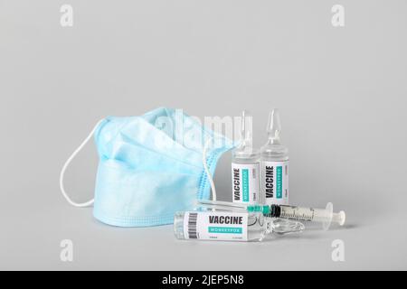 Ampullen mit Monkeypox-Impfstoff und medizinischer Maske auf grauem Hintergrund Stockfoto