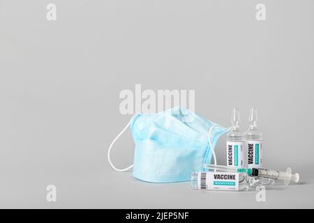 Ampullen mit Monkeypox-Impfstoff und medizinischer Maske auf grauem Hintergrund Stockfoto