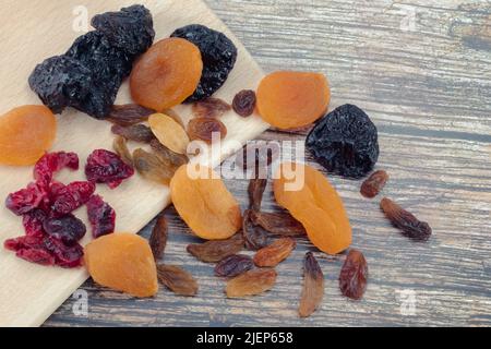 Auswahl an getrockneten Früchten. Getrocknete Pflaumen, Aprikosen, Preiselbeeren, Trauben auf Holztisch. Nahaufnahme. Stockfoto