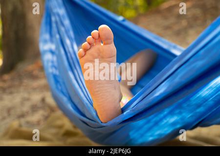 Kinderfuß in einer Hängematte, rollend im Wald im Sommer in der Sonne, Rest in einer Hängematte, ein Fuß in einer Hängematte, Rest im Wald Stockfoto