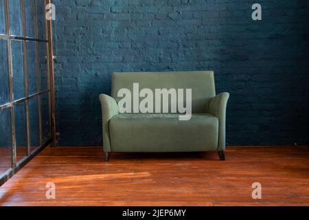 Grünes weiches Sofa in der Nähe der blauen Wand auf dem Holzboden im Zimmer, Polstermöbel in der Wohnung, Sofa im Flur, Minimalismus Stockfoto