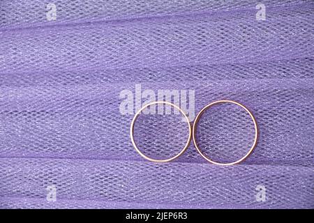 Zwei goldene Eheringe von Braut und Bräutigam liegen auf purpurem Stoff, Eheringen Stockfoto