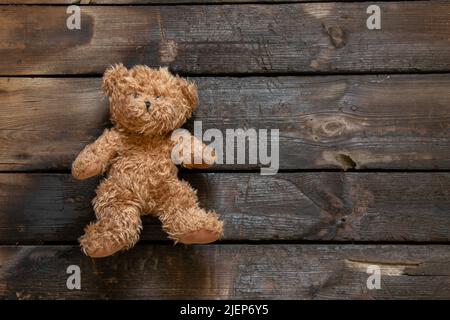 Ein alter Teddybär liegt allein auf einem verbrannten Holzboden, ein Kinderspielzeug auf dem Boden Stockfoto