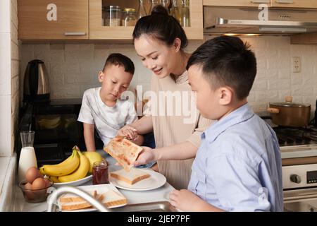 Hände der Mutter lehren Söhne, wie man Marmelade auf Toast zum Frühstück zu spead Stockfoto