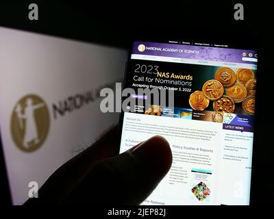 Person mit Mobiltelefon und Webseite der National Academy of Sciences (NAS) auf dem Bildschirm vor dem Logo. Konzentrieren Sie sich auf die Mitte des Telefondisplays. Stockfoto