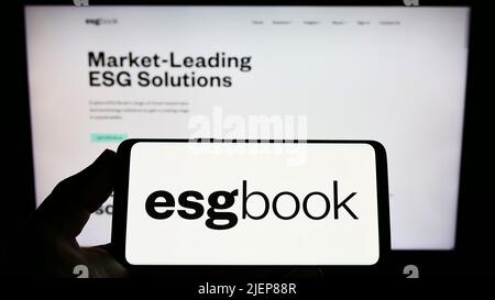 Person mit Smartphone und Logo des britischen Nachhaltigkeitsdatenunternehmens, dem Unternehmen, das sich für Nachhaltigkeitsdaten, das sich auf dem Bildschirm vor der Website aufhält. Konzentrieren Sie sich auf die Telefonanzeige. Stockfoto