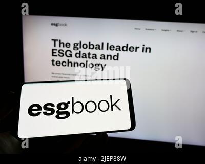 Person, die ein Mobiltelefon mit dem Logo des britischen Unternehmens für Nachhaltigkeitsdaten, dem Unternehmen, das sich mit dem Thema „Nachhaltigkeitsdaten“ beschäftigt, auf dem Bildschirm vor der Webseite hält. Konzentrieren Sie sich auf die Telefonanzeige. Stockfoto