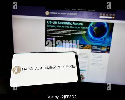 Person, die das Smartphone mit dem Logo der National Academy of Sciences (NAS) auf dem Bildschirm vor der Website hält. Konzentrieren Sie sich auf die Telefonanzeige. Stockfoto