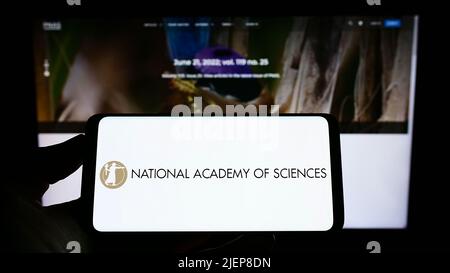 Person, die ein Mobiltelefon mit dem Logo der National Academy of Sciences (NAS) auf dem Bildschirm vor der Webseite hält. Konzentrieren Sie sich auf die Telefonanzeige. Stockfoto