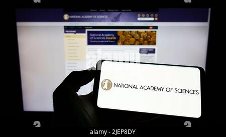 Person mit Mobiltelefon und Logo der National Academy of Sciences (NAS) auf dem Bildschirm vor der Webseite. Konzentrieren Sie sich auf die Telefonanzeige. Stockfoto